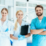 A dentist and two nurses are posing in the dental office on the background of dental equipment.
